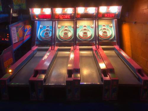 Four skee-ball lanes with colorful scoring displays, illuminated in a dimly lit arcade setting.