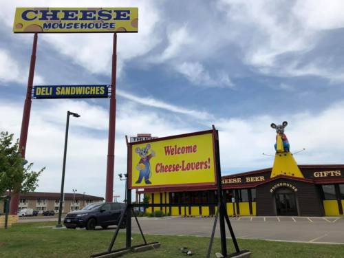 A colorful restaurant sign reads "Welcome Cheese-Lovers" outside the Cheese Mousehouse, featuring a mouse statue.