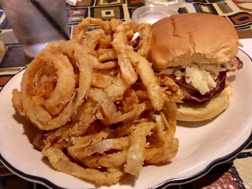 A plate featuring a sandwich with coleslaw and a side of crispy onion rings.