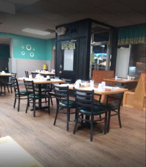 A cozy restaurant interior with empty tables and chairs, featuring wooden floors and teal walls.
