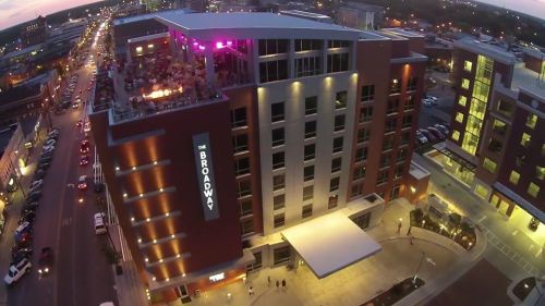 Aerial view of The Broadway building, showcasing its modern architecture and rooftop area, with city streets below.