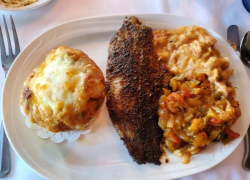A plate featuring seasoned fish, creamy pasta, and a vegetable medley, accompanied by a cheesy baked dish.