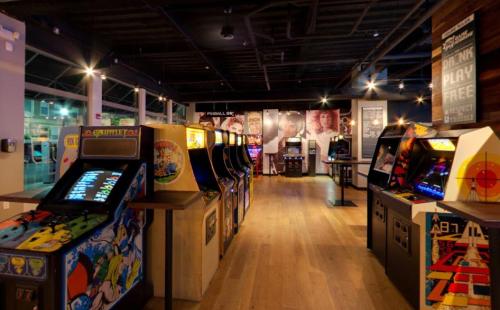 A vibrant arcade with classic game machines lined up, featuring colorful artwork and a lively atmosphere.