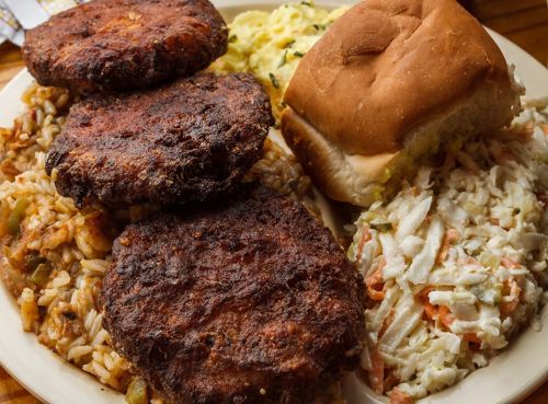 A plate featuring three crispy patties, rice, coleslaw, scrambled eggs, and a soft bun.