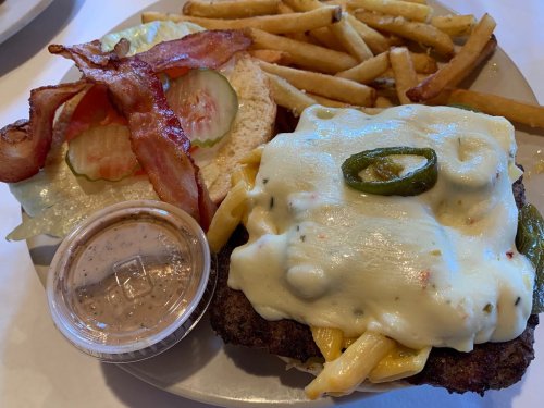 A plate featuring a burger topped with jalapeños and creamy sauce, served with bacon, lettuce, tomato, and fries.
