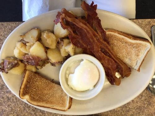 A plate with crispy bacon, toast, poached egg, and seasoned potatoes.