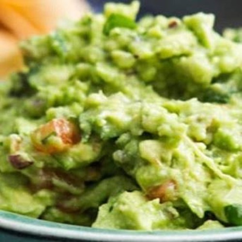 A close-up of creamy guacamole with chunks of tomato and herbs, served in a bowl.