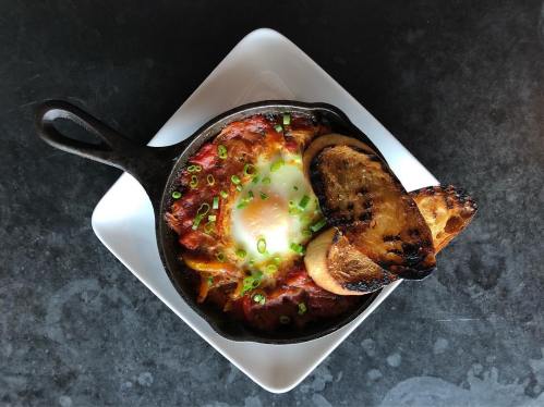 A cast iron skillet with baked eggs in a tomato sauce, topped with green onions and served with toasted bread.