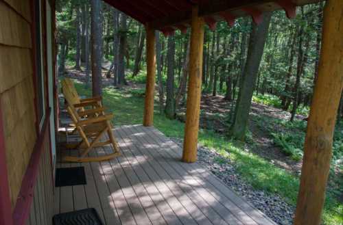 A wooden porch with two rocking chairs, surrounded by trees and greenery in a peaceful forest setting.