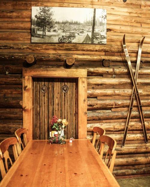 A rustic wooden dining area with a table, floral centerpiece, and vintage skis on the wall beside a wooden door.