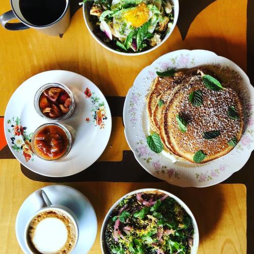 A table spread with pancakes topped with mint, salads, coffee, and jars of preserves on floral plates.