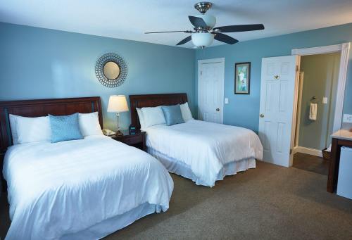 A cozy bedroom with two beds, a ceiling fan, and light blue walls, featuring a nightstand and a bathroom door.