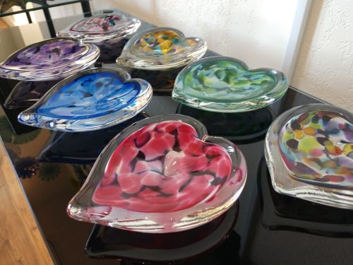 A collection of colorful glass heart-shaped dishes displayed on a black surface.