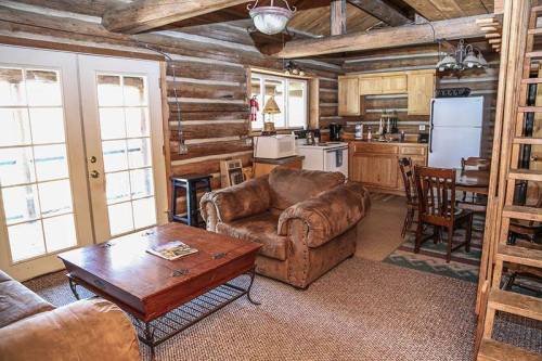 Cozy log cabin interior featuring a living area with a sofa, coffee table, kitchen, and dining space.