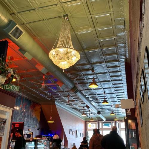 A cozy café interior featuring a decorative chandelier and vintage ceiling tiles, with patrons enjoying the space.