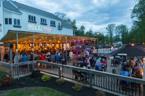 A lively outdoor dining area at Grain Great Bar & Kitchen, filled with patrons enjoying food and drinks under string lights.