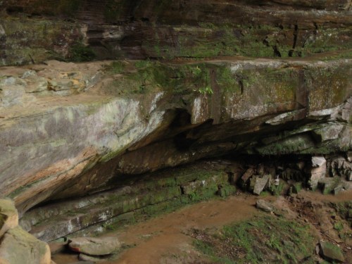 A rocky cave interior with moss-covered walls and a dirt floor, showcasing natural stone formations.