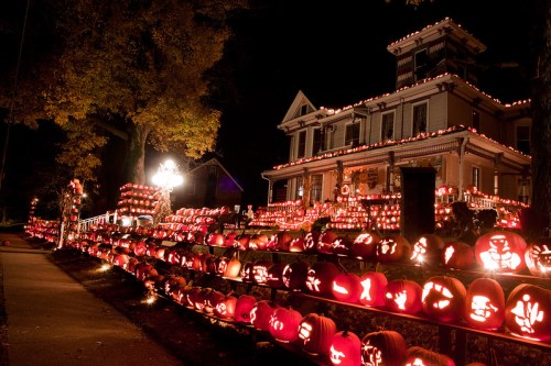 A house decorated with numerous carved pumpkins, glowing warmly at night, creating a festive Halloween atmosphere.