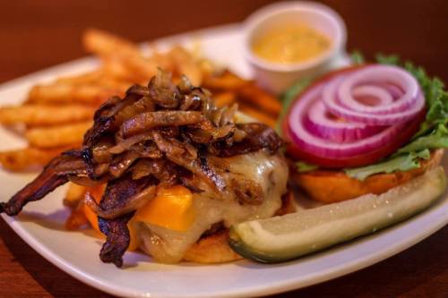 A juicy burger topped with melted cheese, sautéed onions, lettuce, and red onion, served with fries and a pickle.