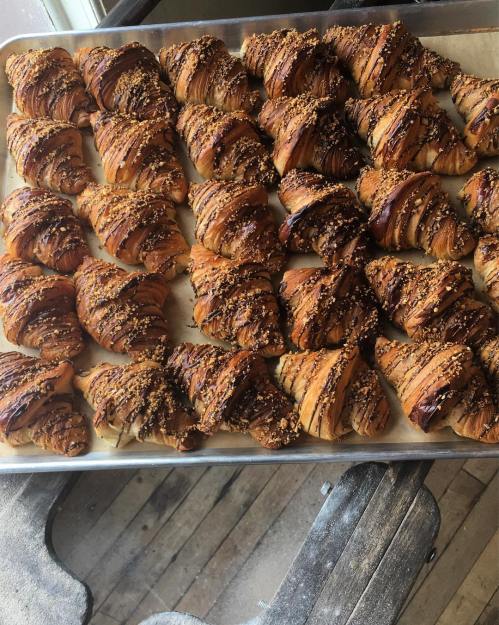 A tray of freshly baked, golden-brown croissants topped with chocolate and sprinkled with nuts.
