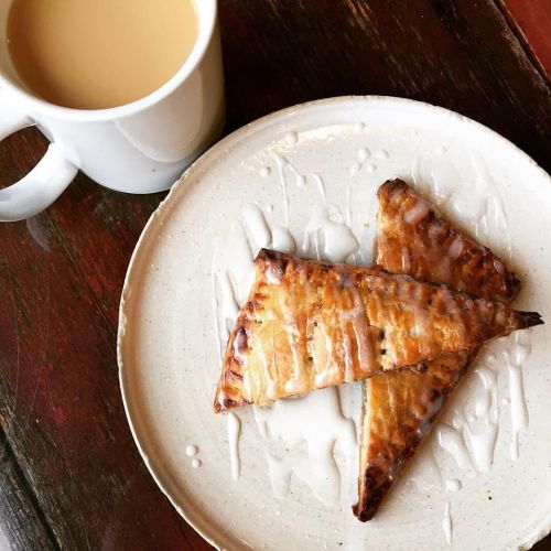 A plate with two golden-brown pastries drizzled with icing, next to a white mug of coffee.