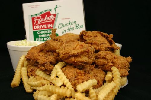 A pile of crispy fried chicken pieces on a bed of crinkle-cut fries, with a takeout box in the background.