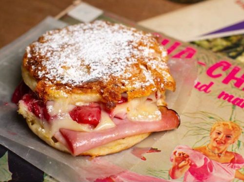 A delicious sandwich with ham, cheese, and strawberries, dusted with powdered sugar, on a vintage magazine backdrop.