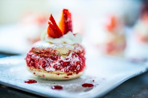A close-up of a red velvet dessert with whipped cream and strawberries, served on a white plate.