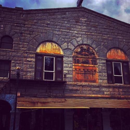 Weathered stone building with arched windows, rusted details, and a vintage sign displaying the year 19__.