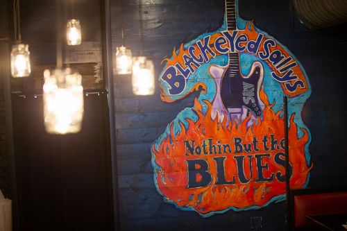 Colorful mural of a guitar with flames, featuring the text "Black Eyed Sally's Nothin' But the Blues" on a dark wall.