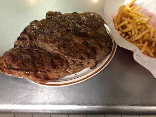 A large, grilled steak on a plate next to a serving of golden French fries.