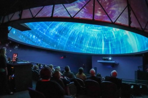A planetarium with an audience watching a starry sky projection on a dome ceiling.