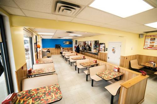 A bright, casual dining area with colorful tables, empty seats, and a counter in the background.