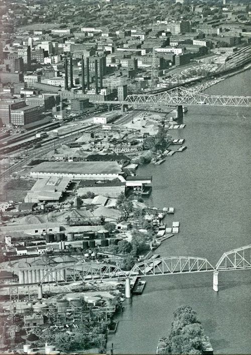 Aerial view of a cityscape with a river, bridges, and industrial buildings along the waterfront.