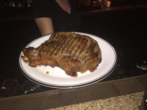 A large, grilled steak on a white plate, served at a restaurant, with a dark background.