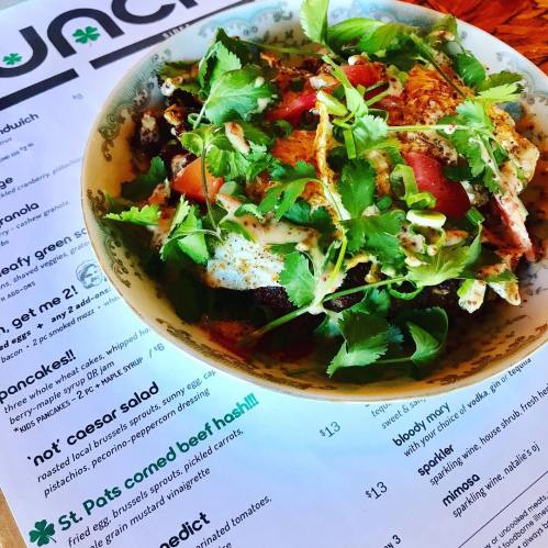 A colorful bowl of corned beef hash topped with cilantro and tomatoes, next to a menu featuring various dishes.