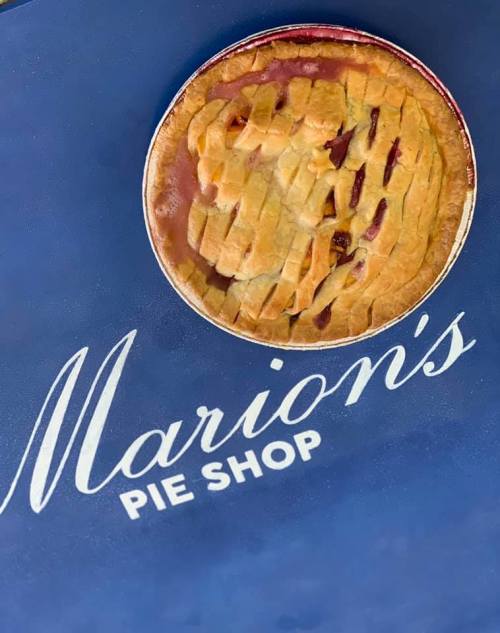 A freshly baked pie with a lattice crust sits on a blue surface featuring "Marion's Pie Shop" logo.