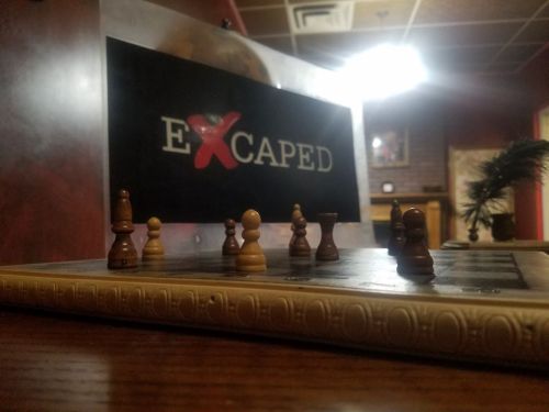 A close-up of a chessboard with pieces in focus, set against a backdrop featuring the word "EXCAPED."