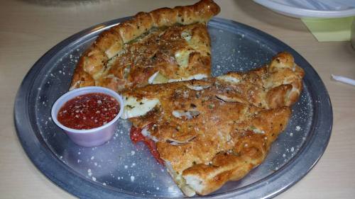 Two large calzones on a silver platter, sprinkled with herbs, served with a side of marinara sauce.