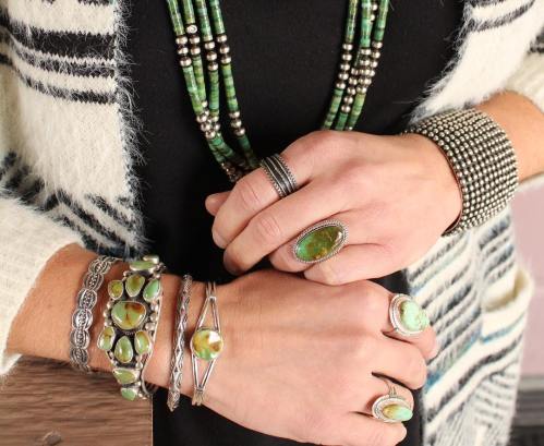 Close-up of hands adorned with various silver and green stone jewelry, including rings, bracelets, and a necklace.