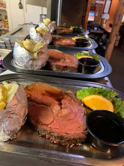 Plates of sliced roast beef with baked potatoes, salad, and dipping sauce, arranged in a restaurant setting.