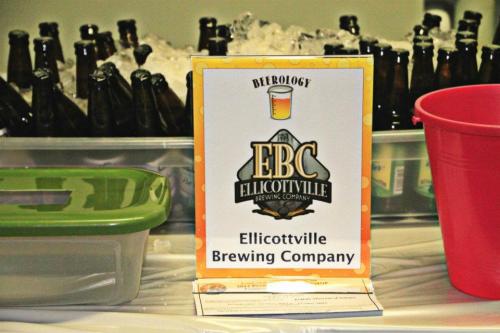 Sign for Ellicottville Brewing Company displayed next to bottles and ice, with a green container and a red bucket.