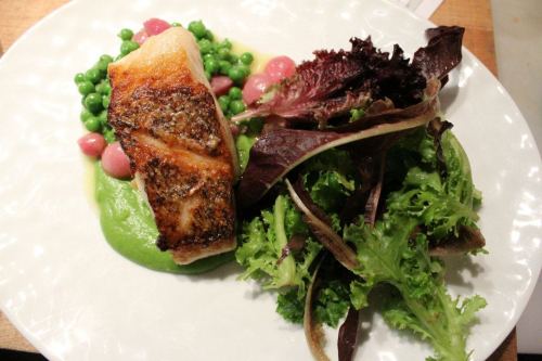A plate featuring seared fish, green peas, pink beans, and a side of mixed greens on a white dish.