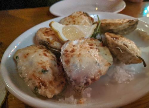 A plate of baked oysters topped with cheese and herbs, garnished with a lemon wedge, served on a bed of rice.
