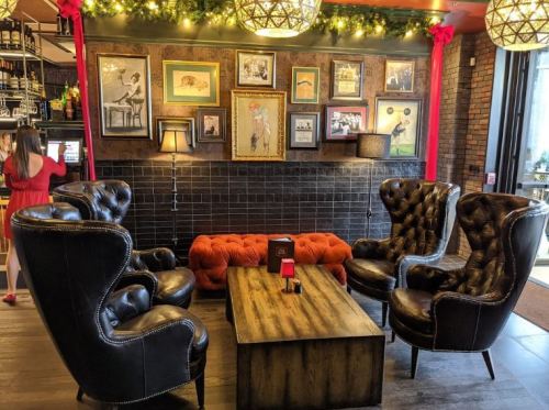 Cozy lounge area with black leather chairs, a wooden table, and framed artwork on the wall, decorated with string lights.