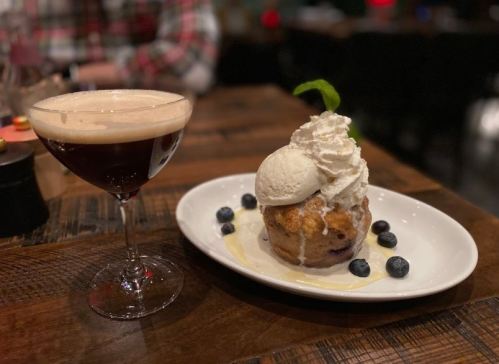A dessert with ice cream and blueberries beside a cocktail in a glass on a wooden table.