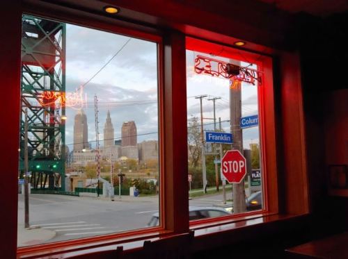 View from a restaurant window featuring city skyline, street signs, and a red neon light.