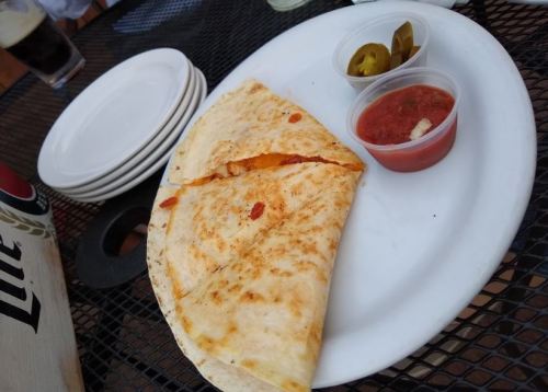 A plate with a folded quesadilla, salsa, jalapeños, and stacked white plates in the background.
