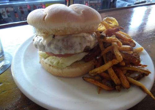 A cheeseburger with lettuce and tomato on a plate, accompanied by a side of crispy fries.