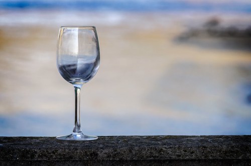 A clear wine glass stands on a ledge with a blurred background of soft colors.
